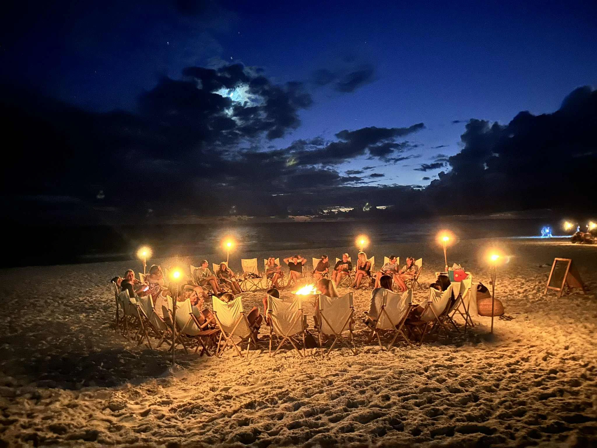 A ring of beach chairs and torches around a bonfire on 30A at night